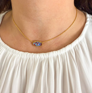 Gold necklace with a colorful pendant worn by a person in a white top.