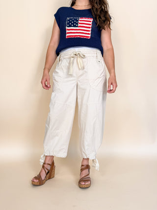 Person wearing a navy blue top with an American flag design and white pants on a beige background