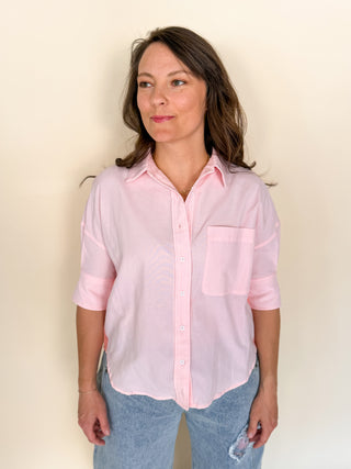 Woman wearing a light pink button-up shirt and blue jeans against a beige background