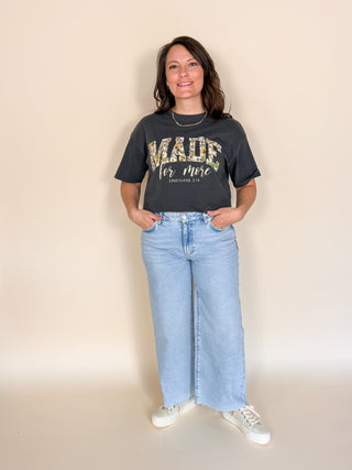 Woman wearing a 'Made for more' t-shirt and blue jeans against a beige background
