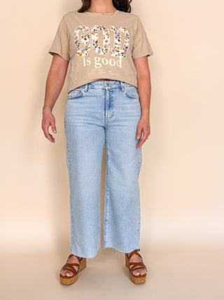 Person wearing a beige t-shirt with text and light blue jeans on a beige background