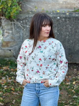Woman wearing a floral sweatshirt and jeans standing outdoors.