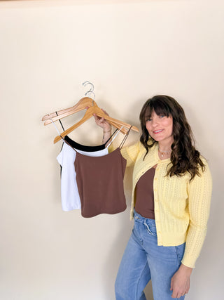 Woman wearing soft core everyday essential cami layered under yellow cardigan with basic camis on hangers